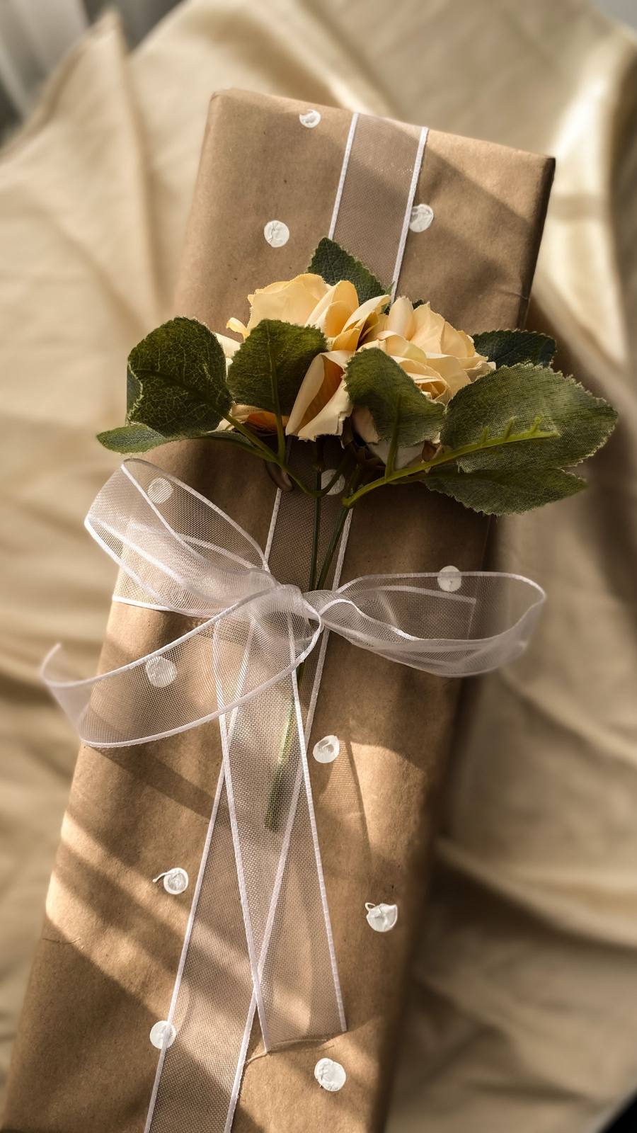 Längliches Geschenk in Kraftpapier mit Schleife und Blumen